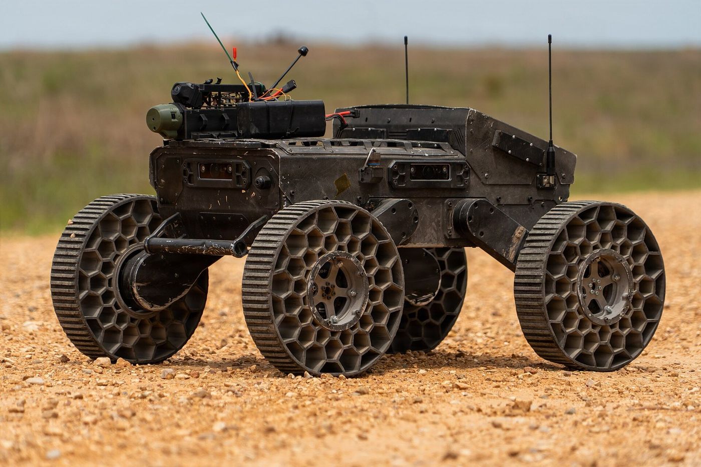 A six-wheeled unmanned ground vehicle on open ground, away from any prepared surface.