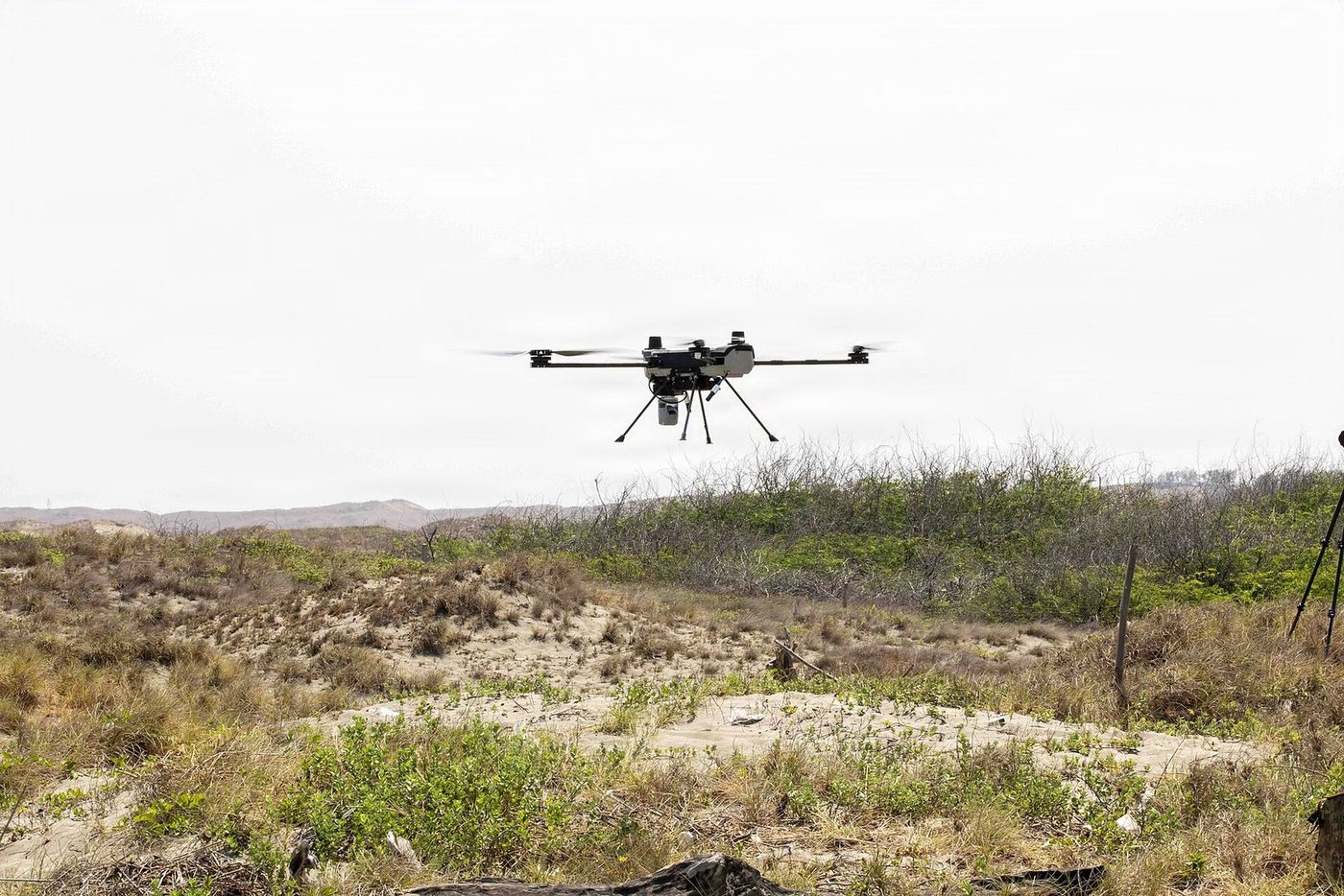 A multicopter holding position over open terrain, working away from any prepared site.