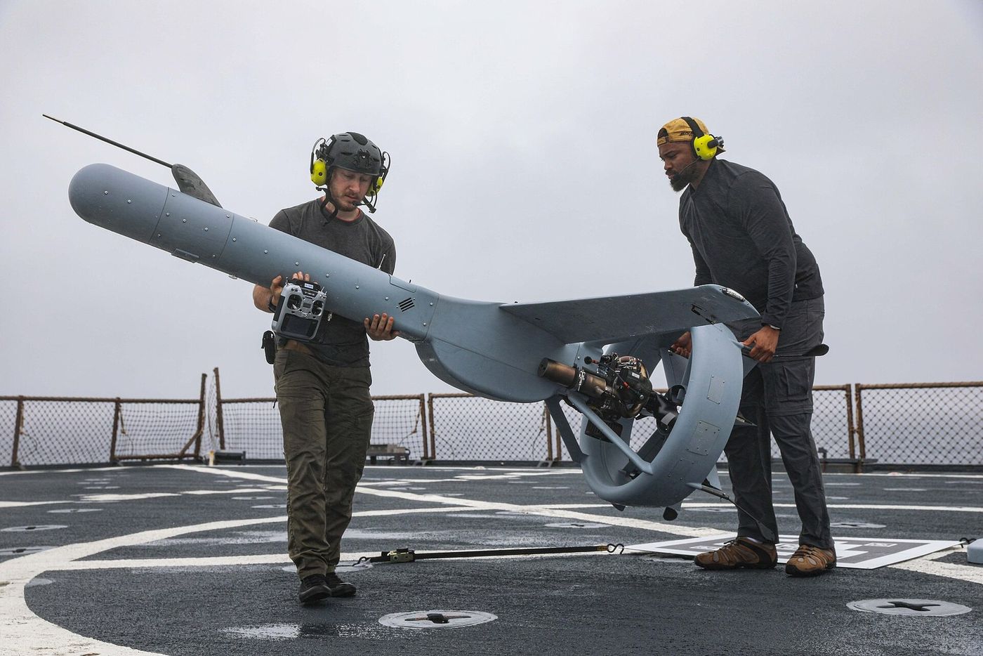 Two crew handling a fixed-wing unmanned aircraft before launch.