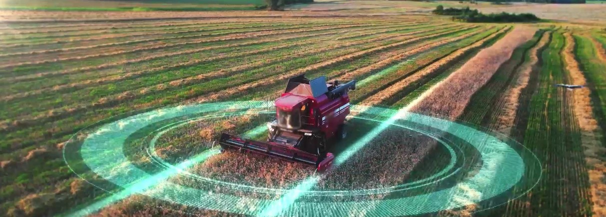 Aerial view of a harvester working a field, with concentric rings marking a precision positioning footprint.
