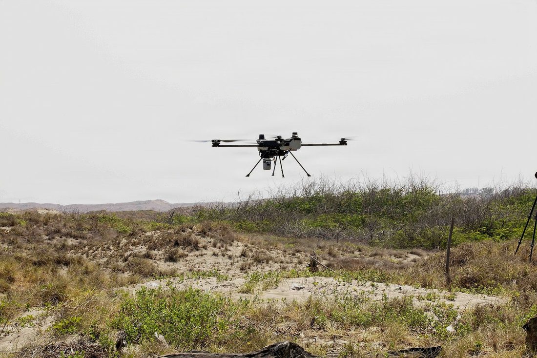 A multicopter holding position over open terrain, away from any prepared site.